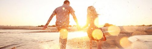couple holds hands walking along beach in beautiful sunny sky