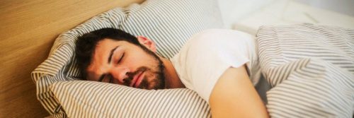 man sleeps tightly on bed covering body with stripped blanket