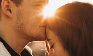 man kissing girlfriend forehead in sunny sky