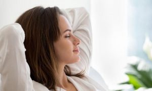 woman eyes closed sits in living room hands over head focusing on inner peace