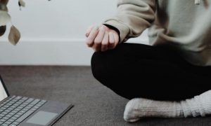 person legs crossed meditate beside laptop plant pot