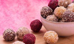 healthy food bowl bliss balls on wood chopping board in pink background