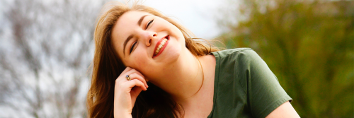 young woman eyes closed sits in park smiling enjoying life