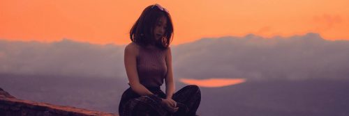 woman sits legs crossed on rock thinking in sunset cloudy sky