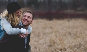 couple happy faces looking smiling in field while man carrying partner