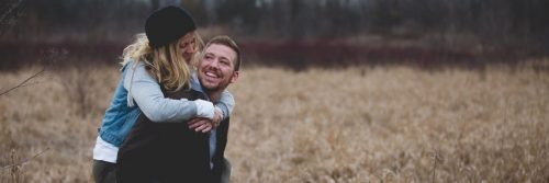 couple happy faces looking smiling in field while man carrying partner