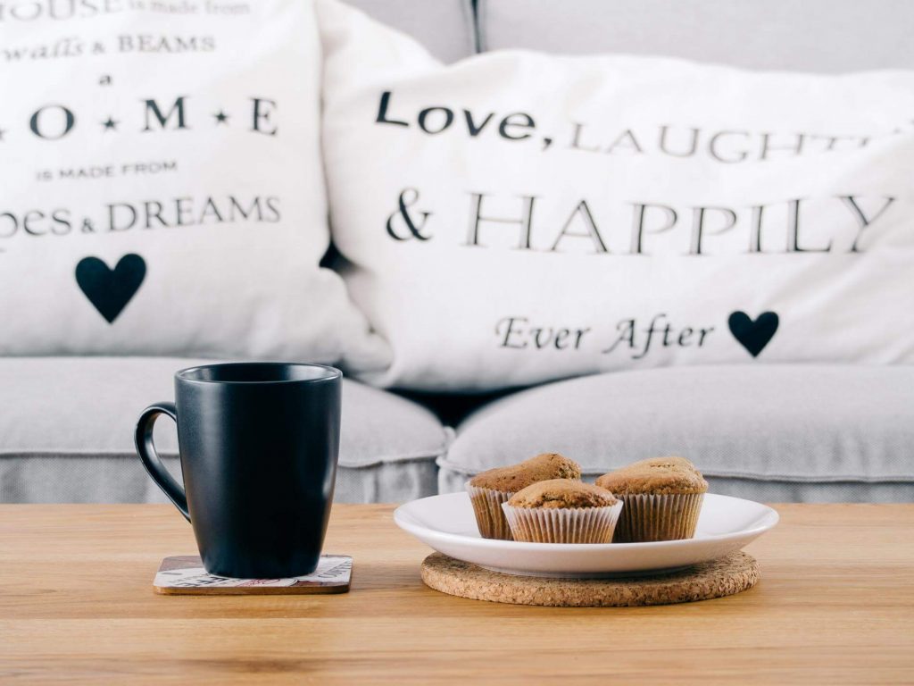 cup cake on white plank next to black mug beside white pillows on couch