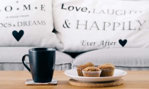 cup cake on white plank next to black mug beside white pillows on couch