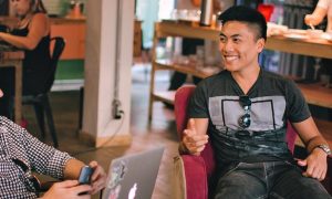 two men sits in busy coffee shop happily talking smiling discussing work