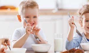 three kids happily sits eating healthy food drinking milk