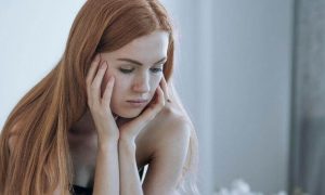 woman sad face hands on cheek sitting in bedroom thinking