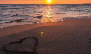 heart symbol on sand beside blue ocean in sunset sky