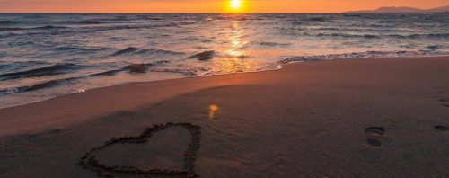 heart symbol on sand beside blue ocean in sunset sky