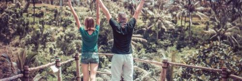 couple stands on bridge in forest raising hands gratitude life