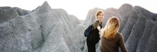 two women climb rocks in shining sky