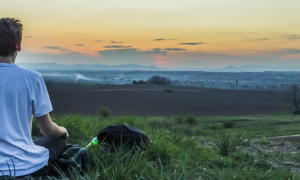 man sits on grass concentrates on meditation breathing in sunset sky
