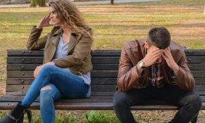 couple sits on bench having conflict while man hands in face upset