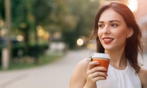 woman stands on street holding coffee cup smiling