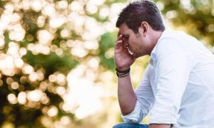 man tiredly sits hand in face thinking in sunny sky