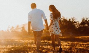 couple holds hands walking on field in sunny sky