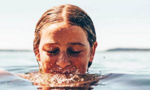 young woman eyes closed swimming ocean water in cloudy sky