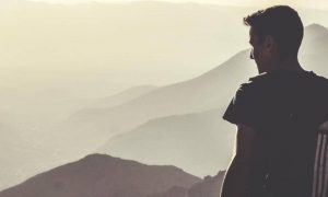 man wearing addidas back bag stands on mountain top looking in foggy sky