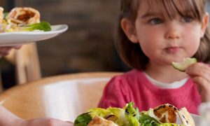 little adorable girl sits beside healthy vegetable dishes eating vegetable cucumber