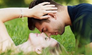 woman lies on green grass while partner sitting kissing