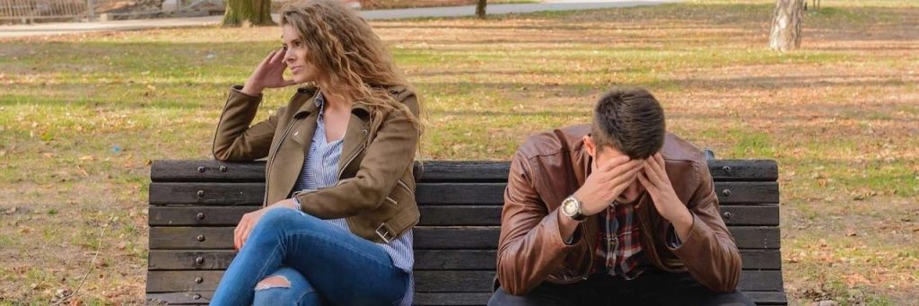 couple sits on bench having conflict while man hands in face upset