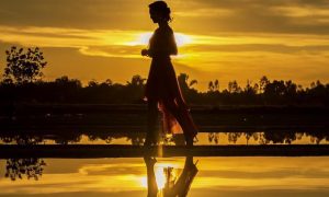 woman walks alone along lake in sunset dark sky