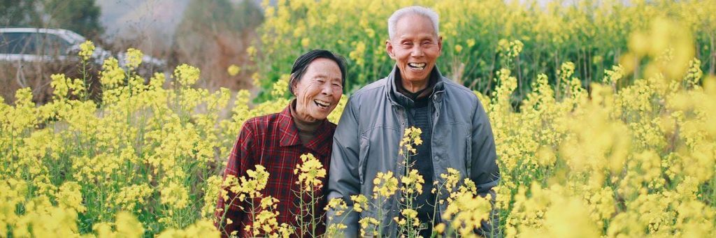 elderly couple stands on field happily smiling