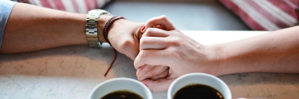 two hands holding beside two black tea cups
