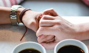 two hands holding beside two black tea cups