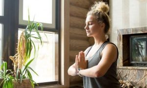woman eyes closed meditate beside plant pots heaters in quiet peaceful living room