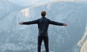 man stands on mountain top facing backward gratitude life