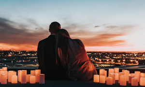 couple sits between candles watching vibration of city while girl lying head on boyfriend shoulder