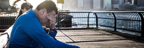 man sits on bench near seaport hand in face feeling sad
