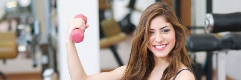 woman happily smiles holding small pink dumbbell exercising in fitness clubs