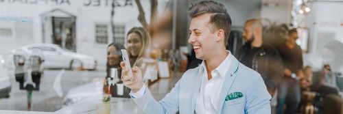 businessman stands outside crowded shop talking on phone smiling happily