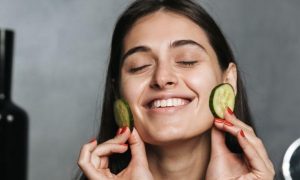 woman eyes closed happily apply cucumber slices on face skin