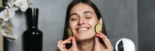 woman eyes closed happily apply cucumber slices on face skin