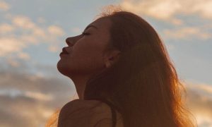 woman eyes closed focuses on breathing in blue cloudy sky