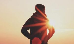 man facing backward stands hand in pock in sunset sky