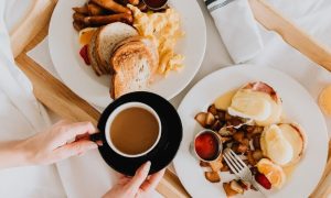 two breakfast dishes on bed drinks coffee juice