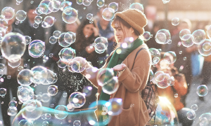 woman stands on street between crowds enjoying bubbles