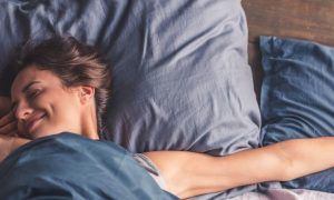 woman wakes up happily smiling stretching up on bed