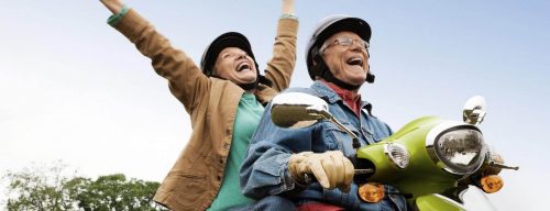 elderly couple rides scooter happily laughs while woman sitting behind raising hand