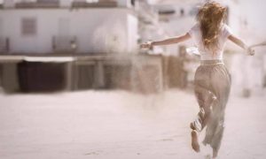 woman facing backward runs on sandy dusty street