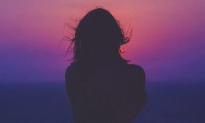 woman facing backward looks at purple blue red dark sky feeling lonely