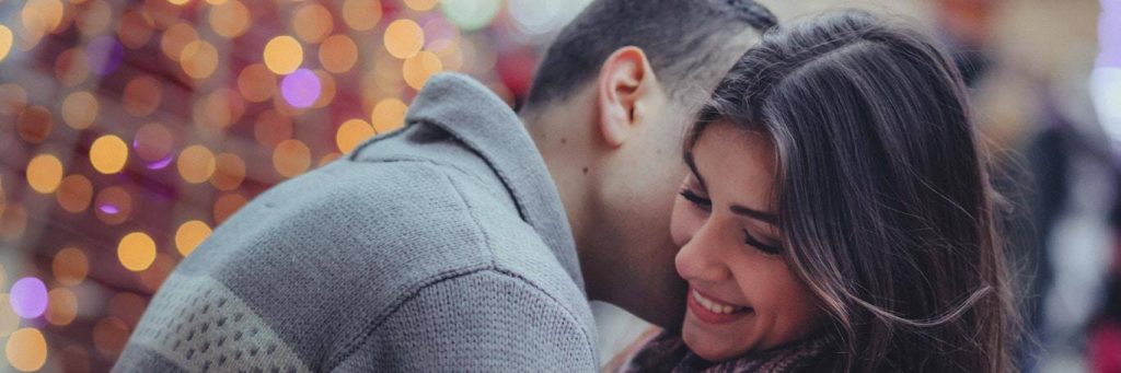 man kisses girlfriend on neck while girl happily smiles